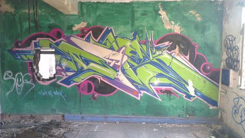 Inside an upstairs room, cracked plaster and peeling floor tiles. The whole wall has been hastily painted in green emulsion and then a clean, wildstyle 