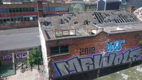Looking down at the side building, the dilapidated roof is missing tiles, the skylights have no glass. One full storey of it is painted with a 'MR WOLF' roller piece