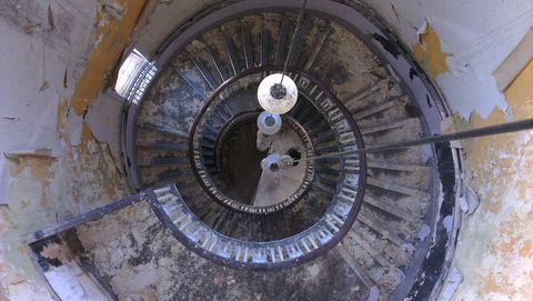 Looking down from the top of a circular tower, a wide spiral staircase descends, winding around ball lamps that hang from the centre. The image is reminiscent of an eye.