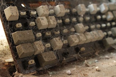 A close up of an old computer keyboard, most of its keys are missing and the few that remain are coated in a fine network of cobwebs.